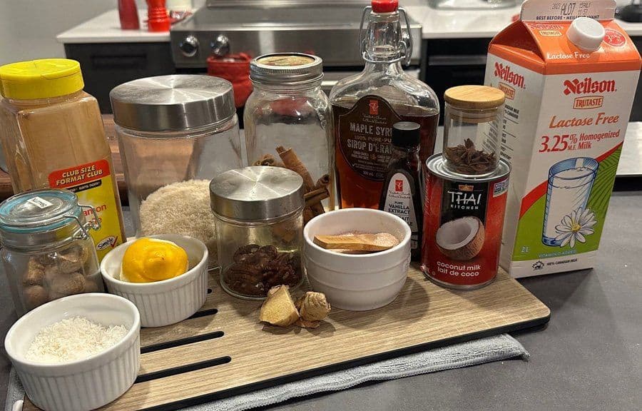 Ingredients for arroz con leche displayed on a wooden board, including rice, milk, maple syrup, coconut milk, lemon, and spices.