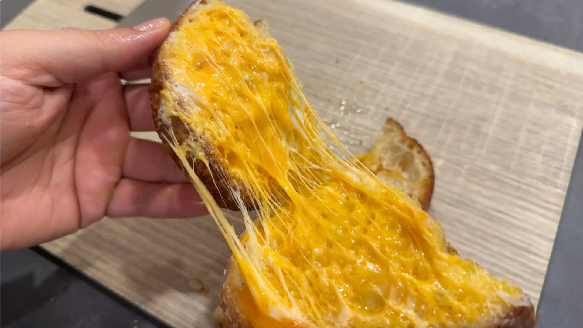 Hand holding a grilled cheese sandwich with melted cheese stretching between two golden-brown toasted bread slices.