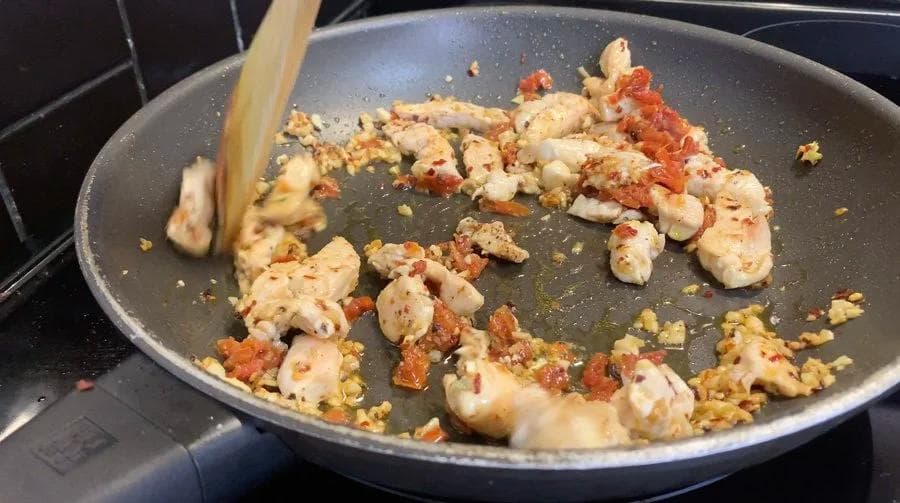 Diced chicken and red peppers being stirred in a non-stick pan with minced garlic and seasonings.