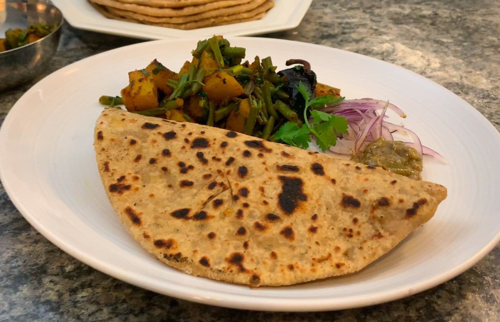 Aloo beans sabji served with roti and garnished with cilantro and pickled onions on a white plate.