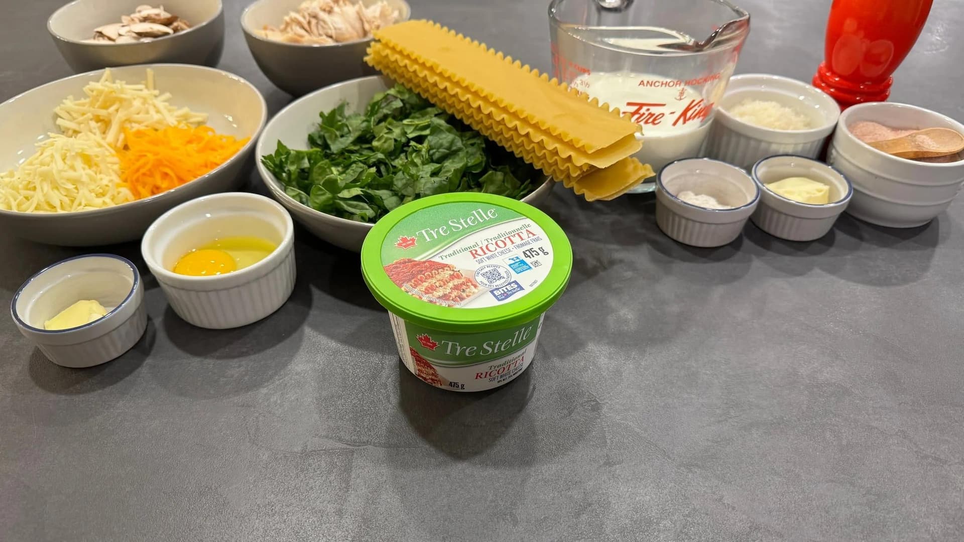 Ingredients laid out for creamy white sauce chicken lasagna including ricotta cheese, pasta sheets, spinach, shredded cheese, and eggs.