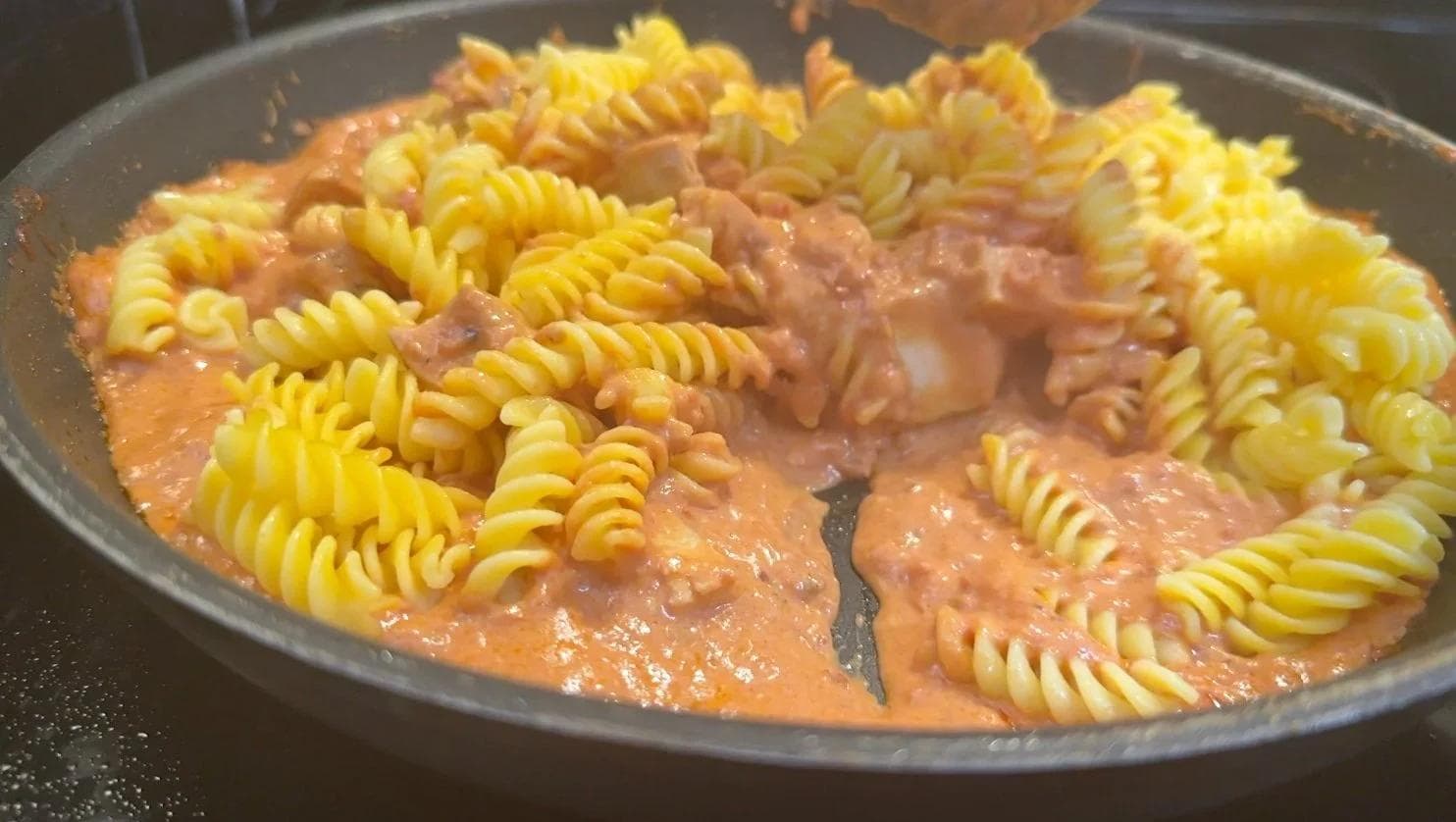 Creamy tomato sauce with diced chicken and spiral pasta in a gray pan, ready for finishing touches.