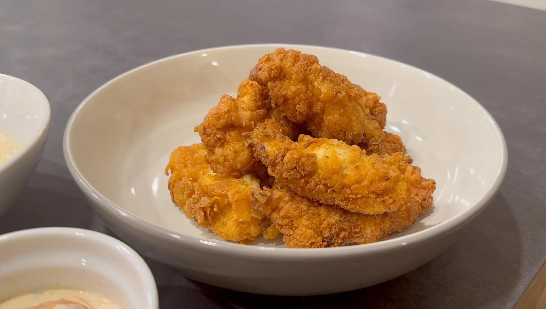 Crispy golden-brown buttermilk fried chicken tenders piled in a white bowl with a crunchy, evenly-fried coating.