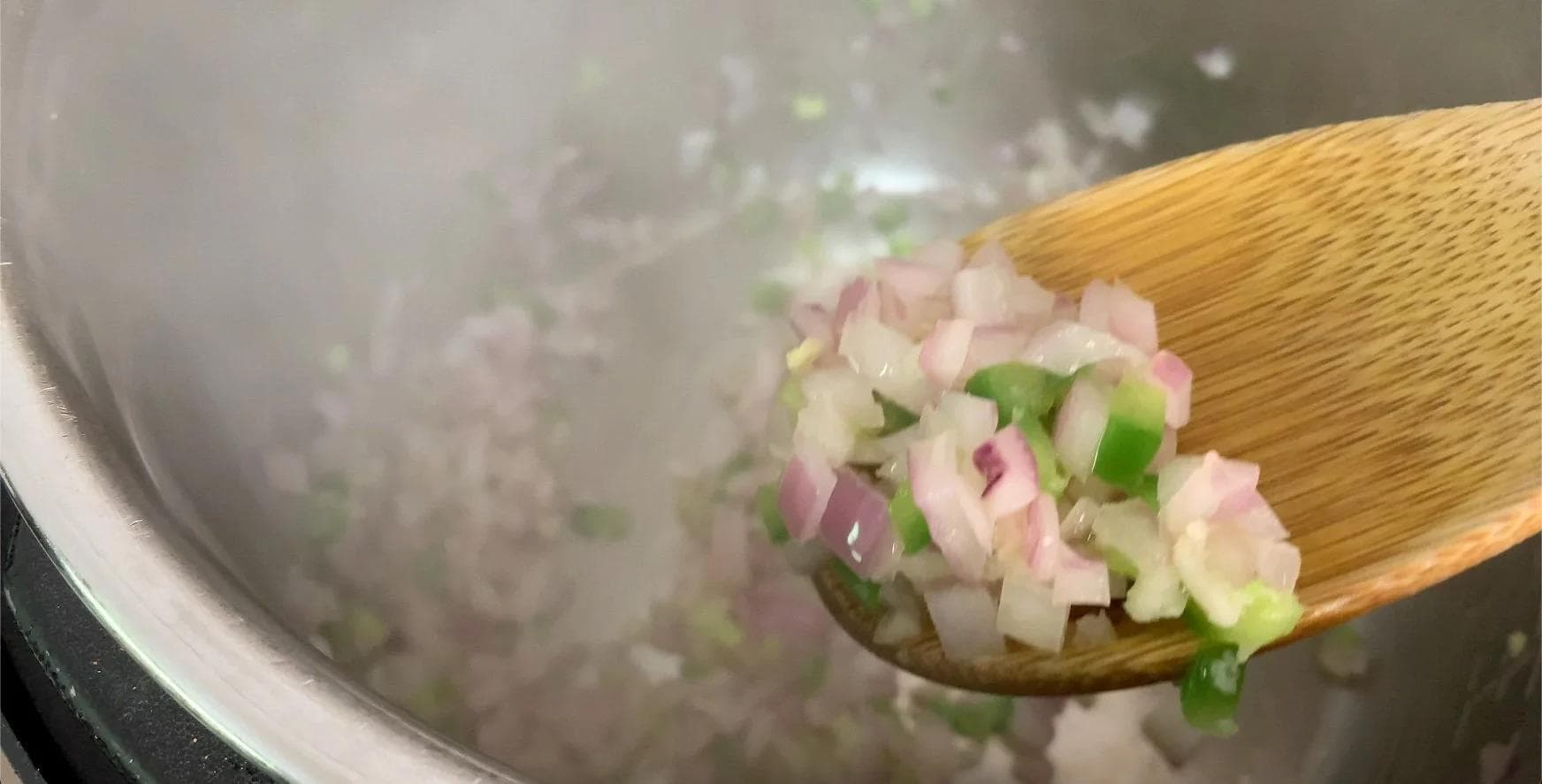 Wooden spoon holding cooked onions, jalapeño, and garlic being added to sautéed ground beef in Instant Pot.