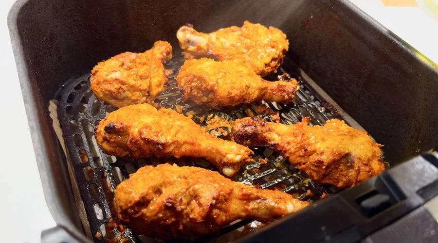 Tandoori chicken pieces in an air fryer basket, golden brown and cooked through, mid-preparation.