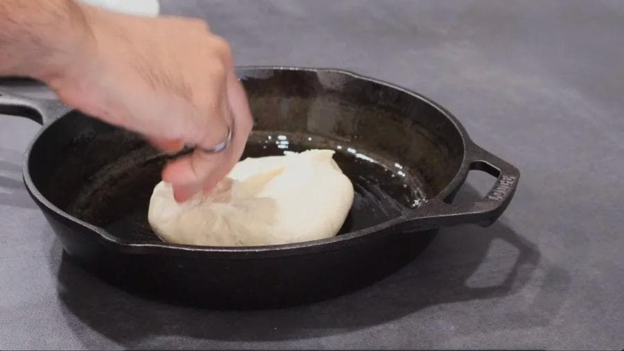 Hands pressing and dimpling pizza dough in an oiled cast iron skillet