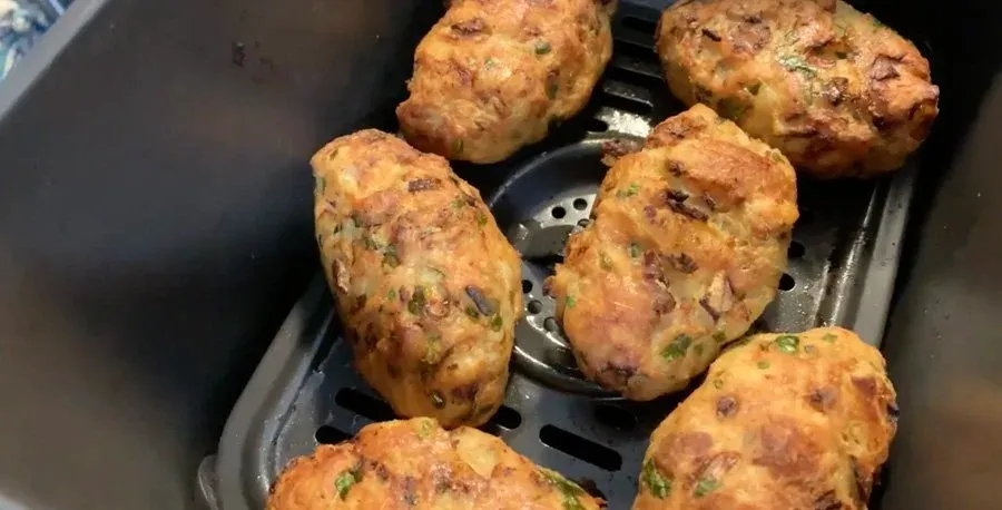 Golden brown and crispy Indian chicken cutlets in an air fryer basket, cooked until golden with herbs visible on the surface.