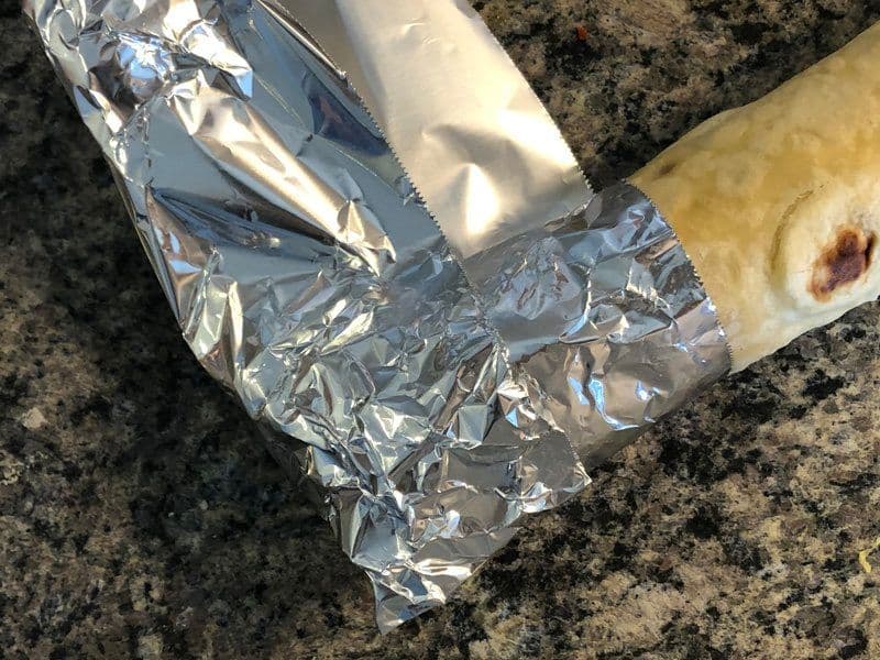 Chicken kathi roll wrapped in aluminum foil on a granite countertop, ready to serve.