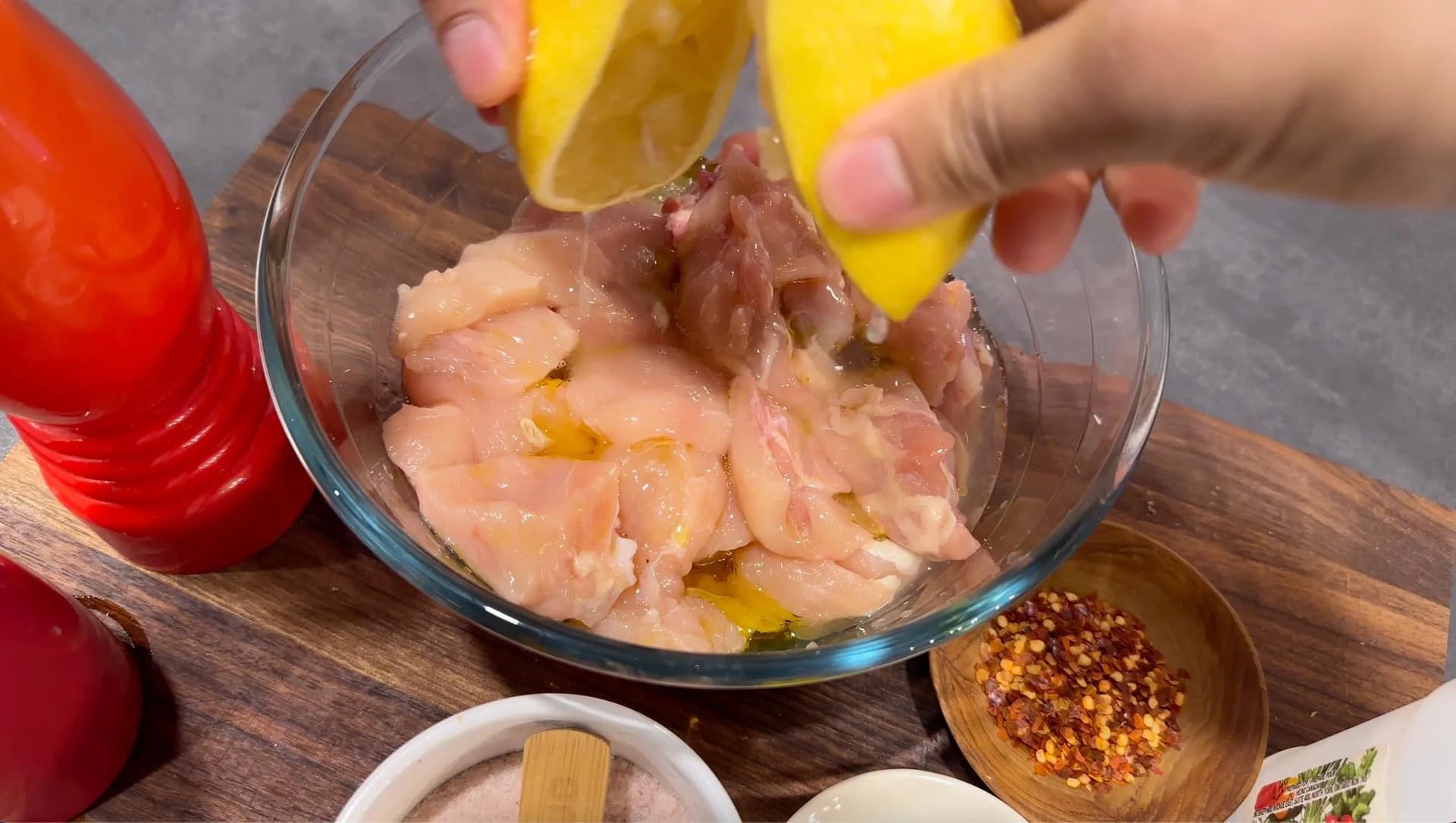 Squeezing lemon juice over cubed chicken in marinade with olive oil and spices in a glass bowl.