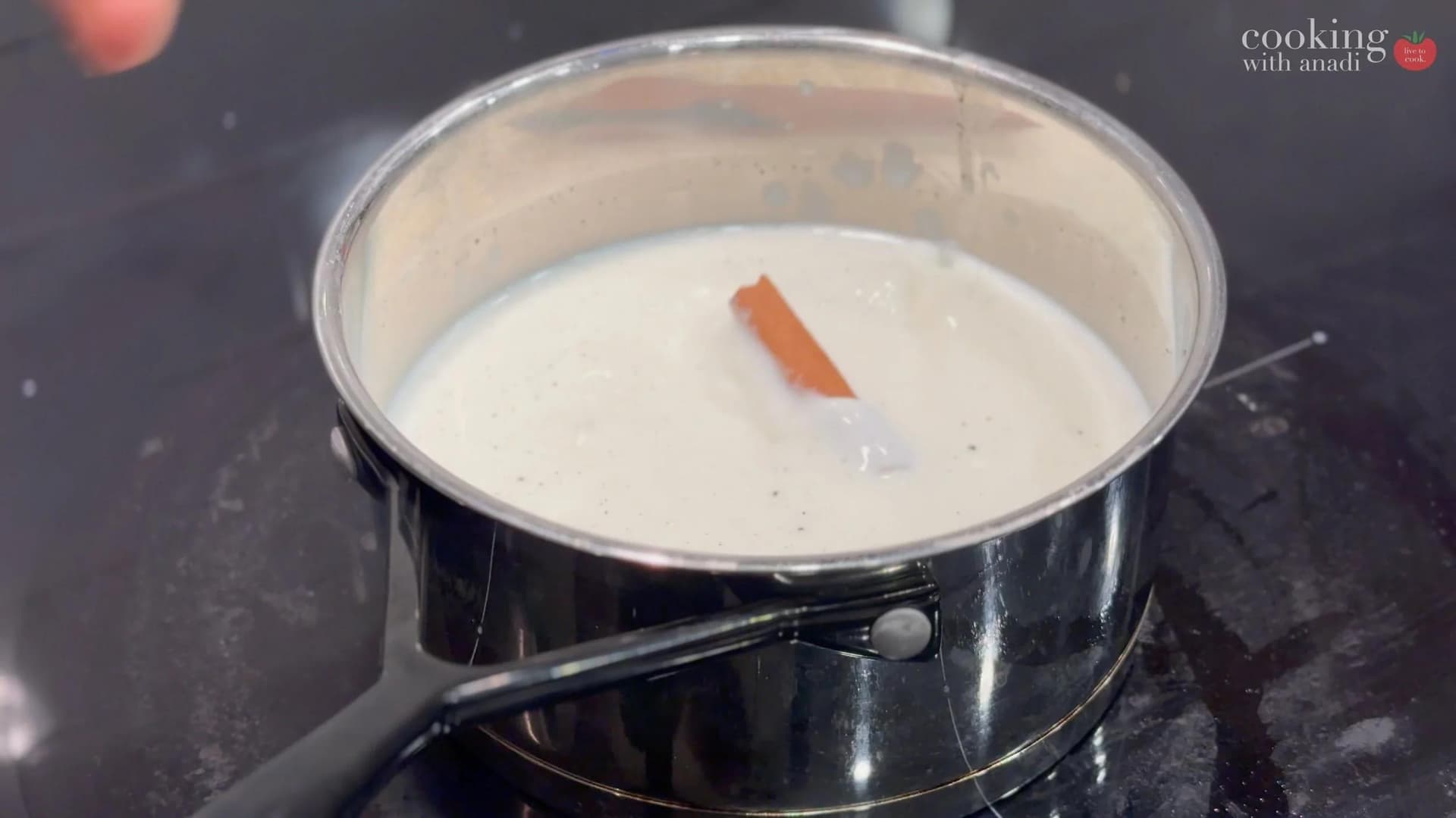 Milk heating in saucepan with vanilla pod and cinnamon stick, just beginning to simmer.