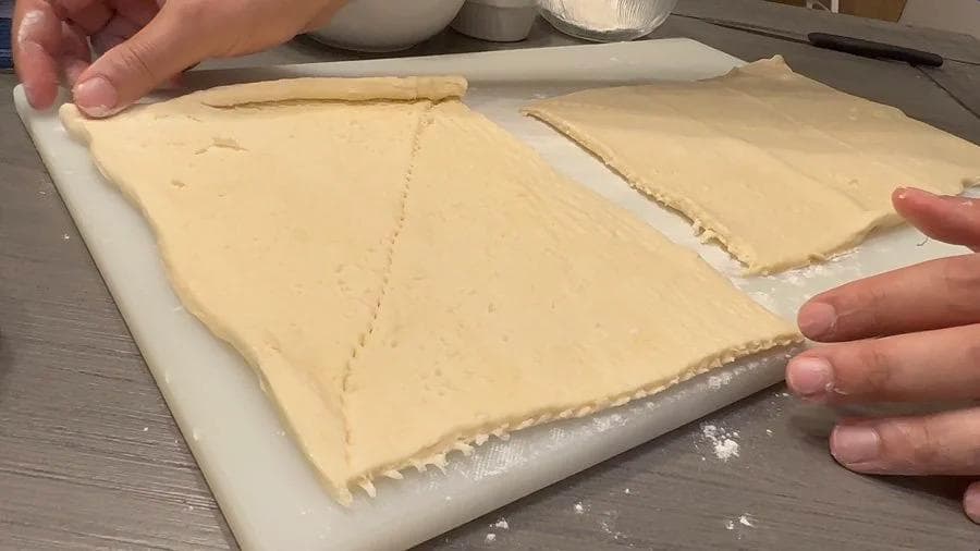 Crescent roll dough cut into thin triangular strips on a white surface, ready for filling.