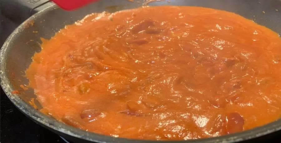 Tomato-based sauce simmering in a pan with visible spices and oil, during the cooking process for Shahi Paneer.