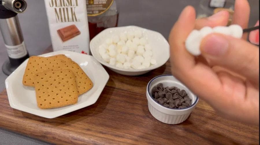 Ingredients for s'mores oatmeal laid out: graham crackers, marshmallows, chocolate chips, and a carton of milk on a wooden surface.