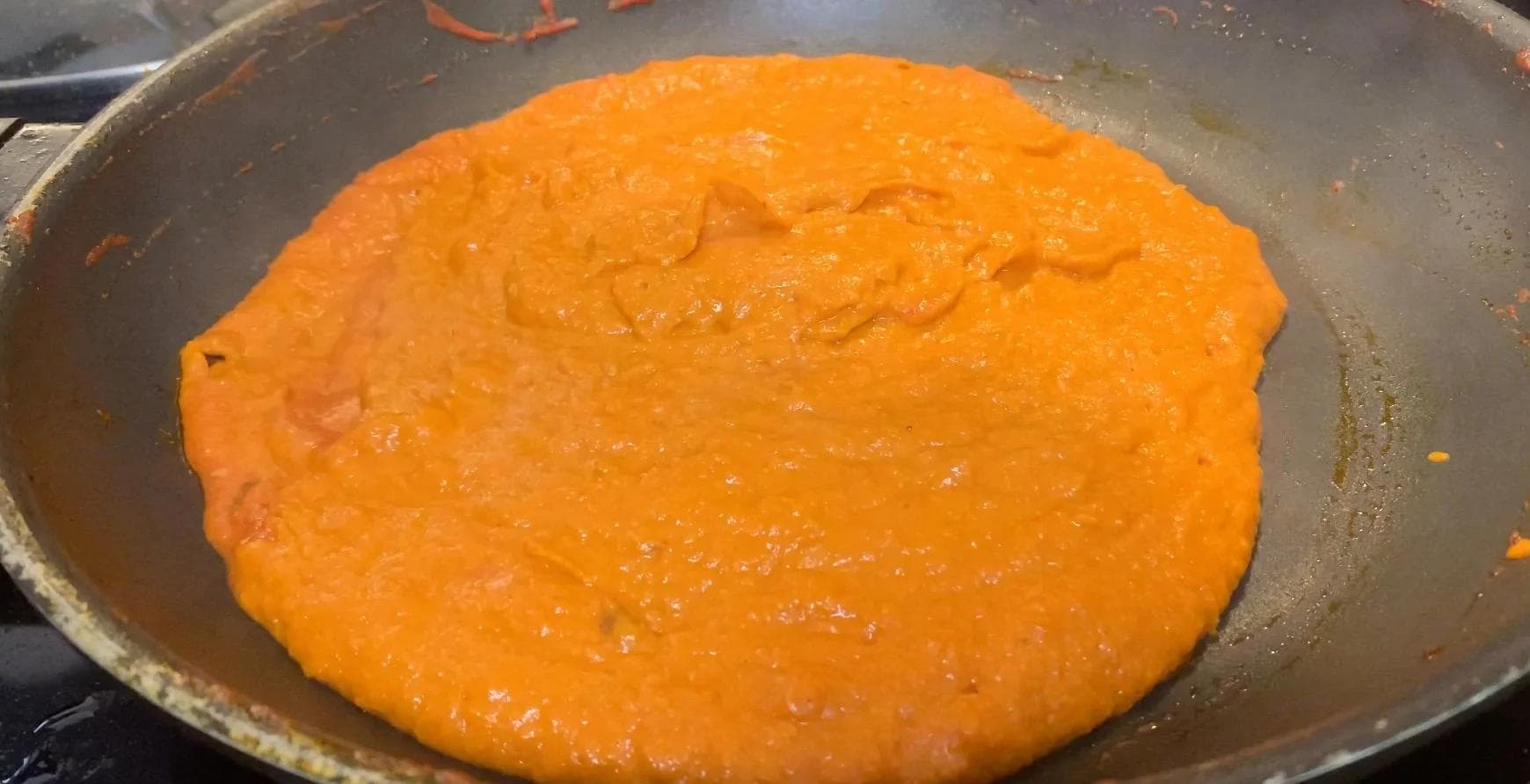 Creamy orange Shahi Paneer sauce simmering in a pan with visible texture and richness.
