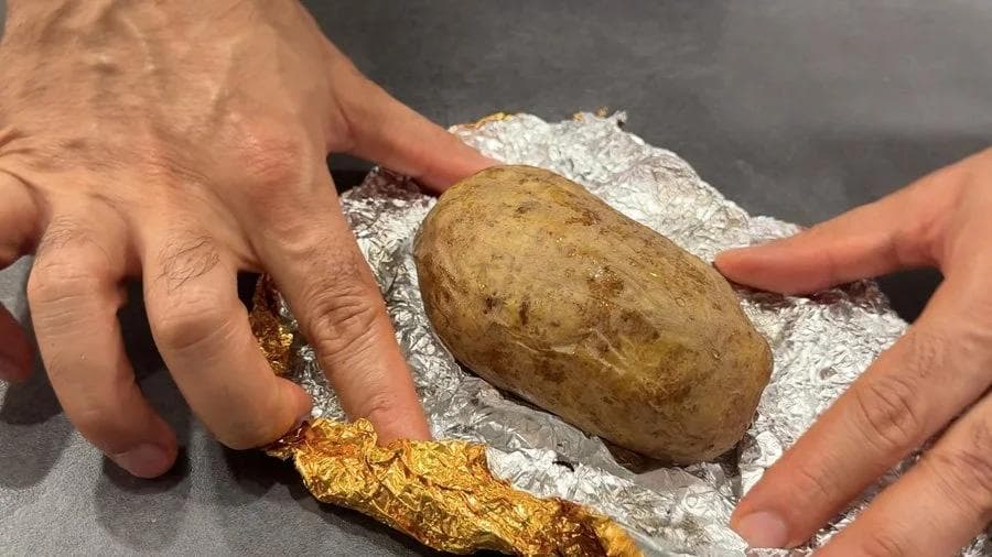 Hands holding a baked potato without foil next to foil-wrapped potato, comparing air fryer cooking results.