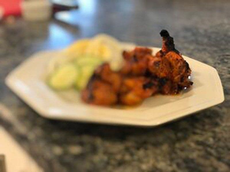 Baked chicken tikka pieces coated in butter sauce served on a white plate with cucumber slices.