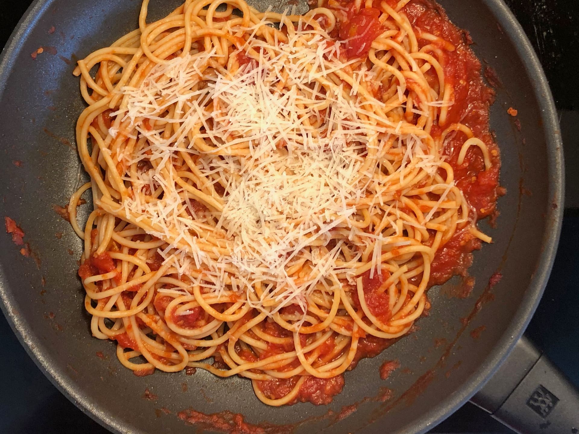 Spaghetti marinara with shredded Parmesan cheese in a skillet, ready to be tossed.