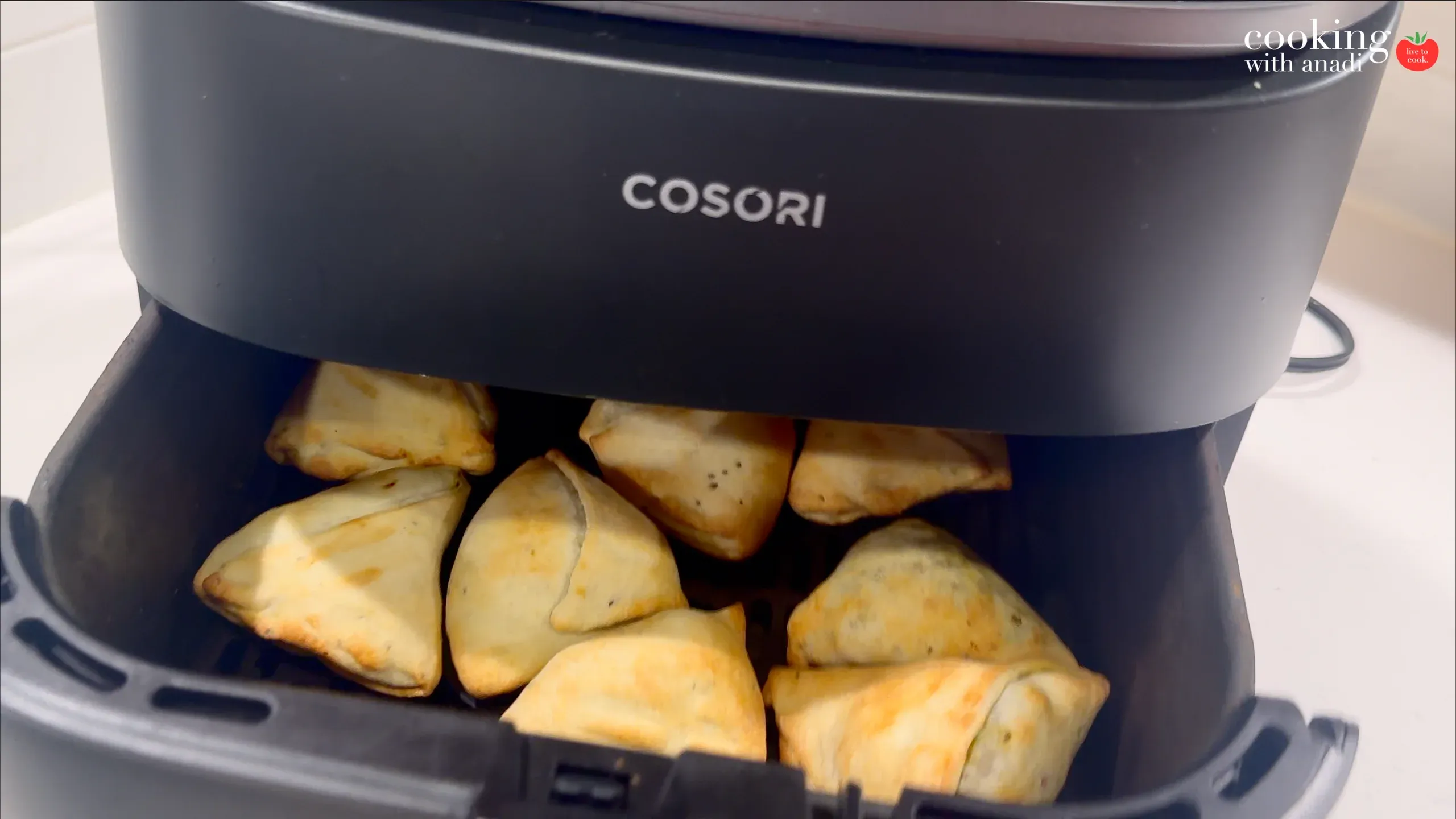 Golden-brown potato samosas in a black Cosori air fryer basket during cooking.