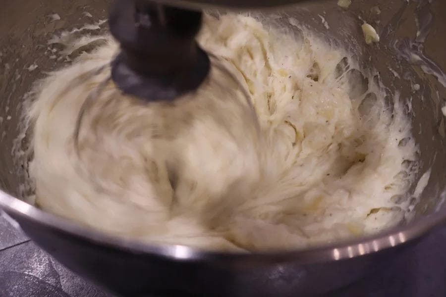 Creamy mashed potatoes being mixed in a stand mixer bowl with a whisk attachment.