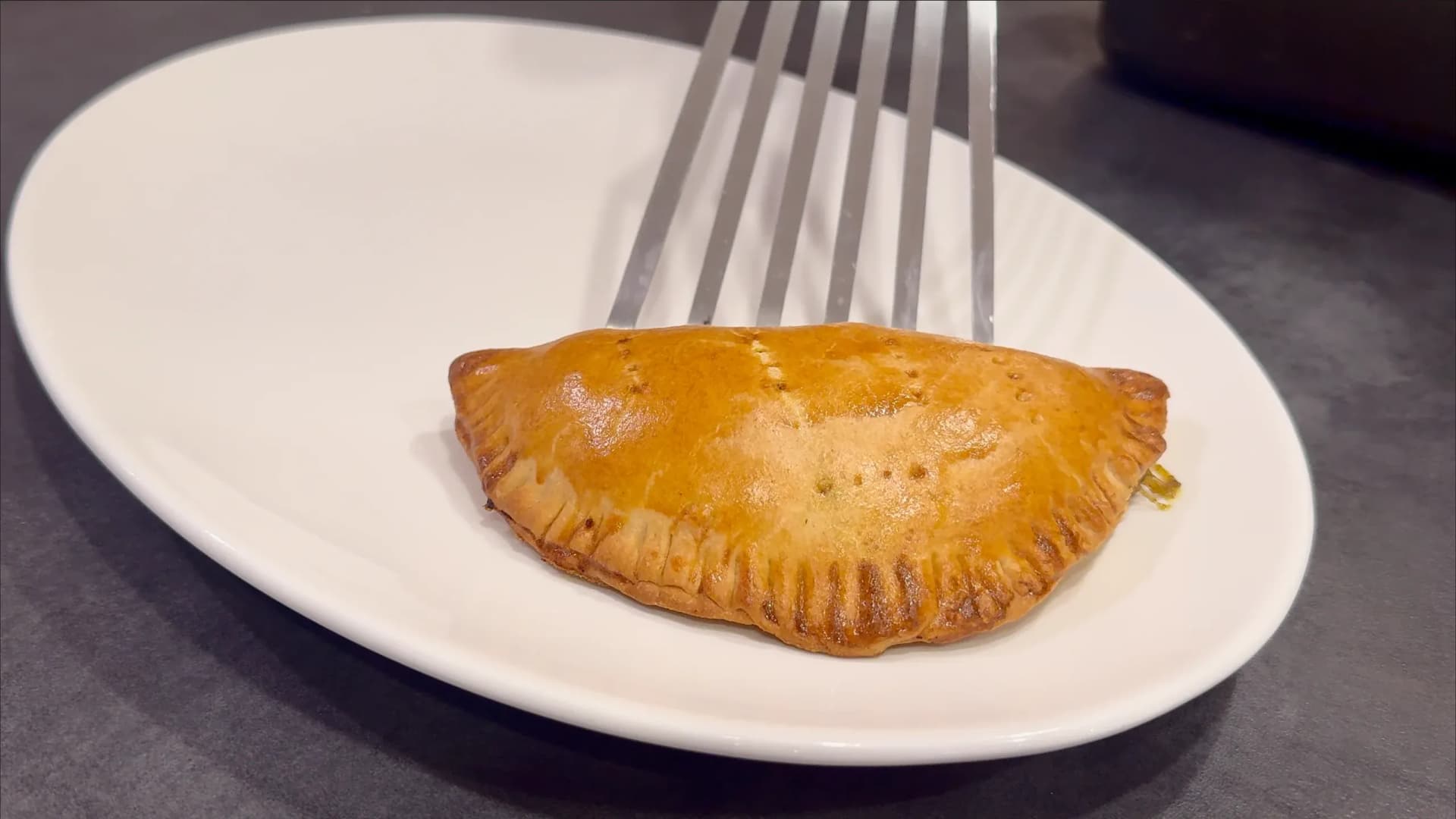 Golden-brown air fryer Nigerian meat pie on a white plate with a fork.