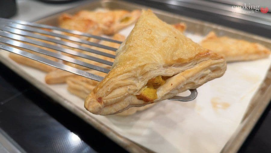 Golden-brown aloo puff pastry on a white plate with a fork, showing the creamy potato filling inside.