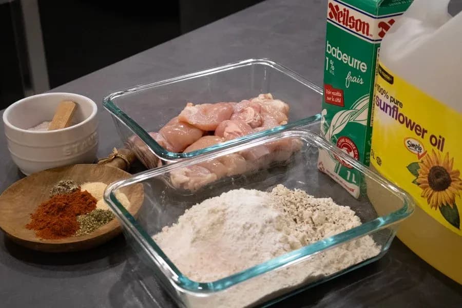 Ingredients for chicken and waffles laid out: raw chicken thighs, flour, spice mix, buttermilk, and sunflower oil.