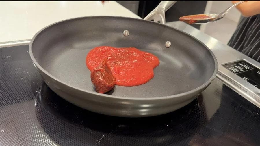 Korean-style sauce simmering in a gray pan, with a spoon drizzling sauce above it.