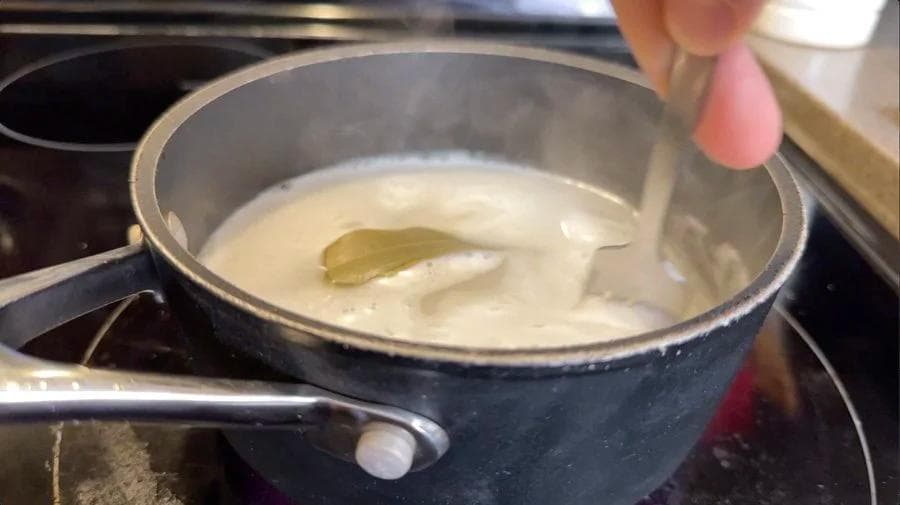 Pot of rice cooking in water with a bay leaf on stovetop, steam escaping from under partial lid.