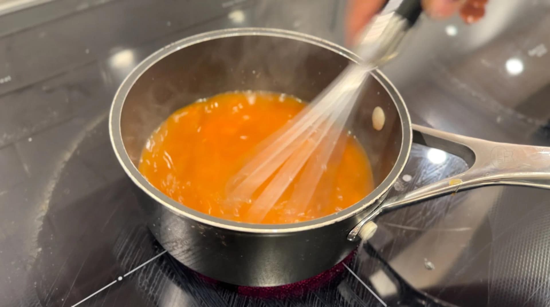 Whisking orange pumpkin sauce in a saucepan on the stovetop until sugar dissolves.