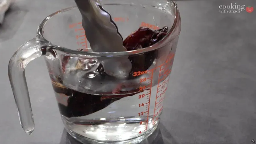 Dried red chiles soaking in water in a glass measuring cup during salsa roja preparation.