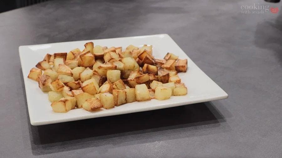 Golden-brown crispy air fryer roasted potatoes cubes served on a white rectangular plate.
