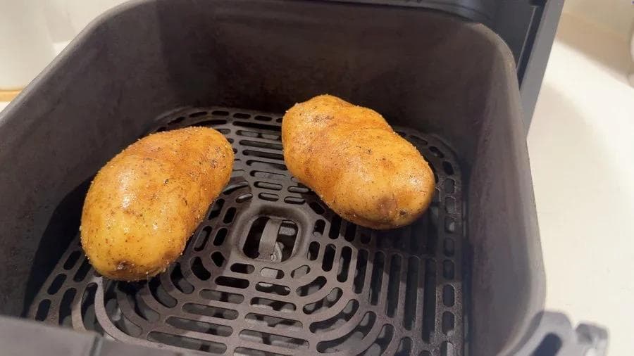 Two golden-brown baked potatoes in an air fryer basket, crisped and ready to cool.
