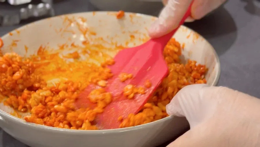 Stirring orange Rice Krispies mixture with a pink spatula in a white bowl.