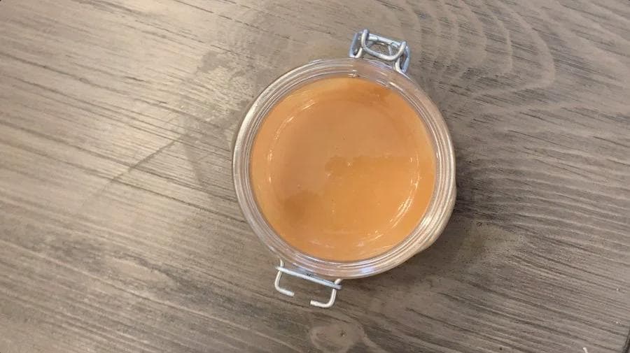 Homemade caramel sauce in a clear glass jar with wire bail closure, showing smooth amber-colored sauce.