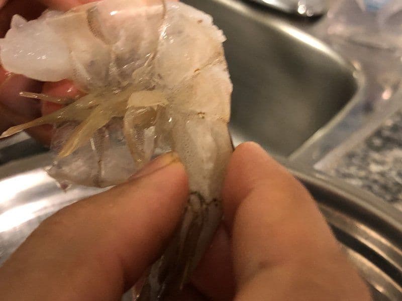 Hand holding a peeled shrimp showing the tail being removed from the cooked shrimp.