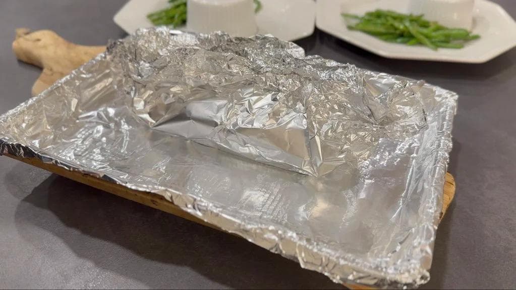 Salmon fillet wrapped in aluminum foil packet on wooden board, ready for baking.