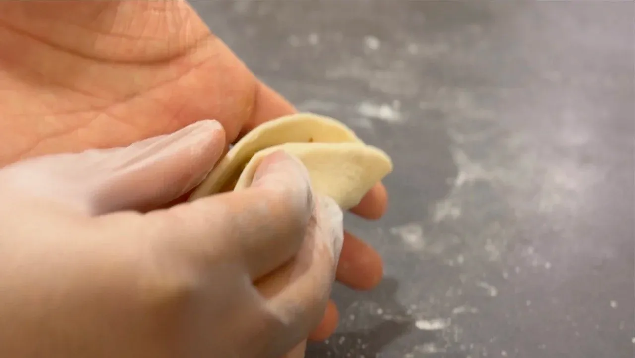 Hand pinching and twisting the top of a momo dumpling to seal the edges closed.