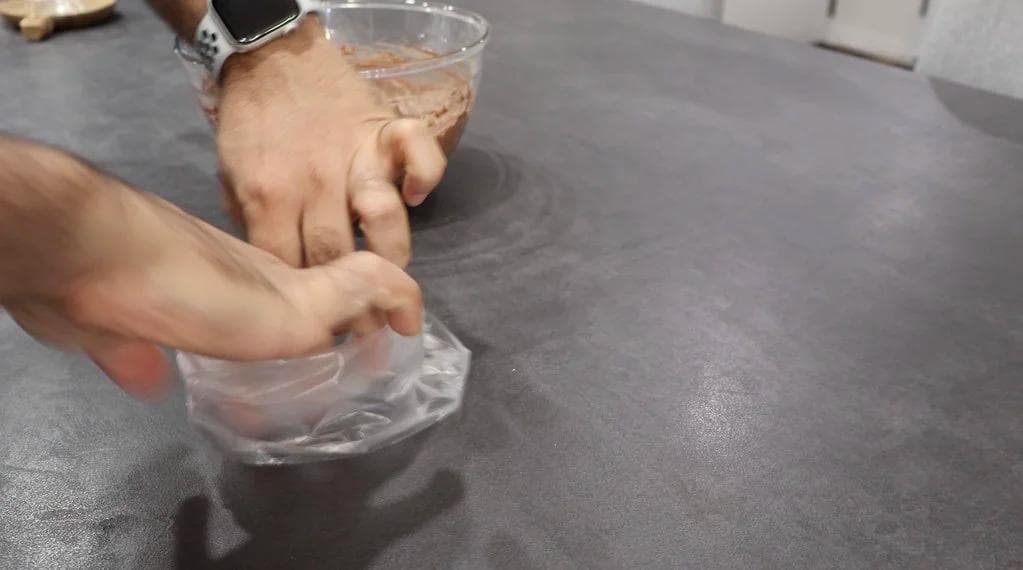Hands transferring whipped cream into a clear piping bag over a gray countertop.