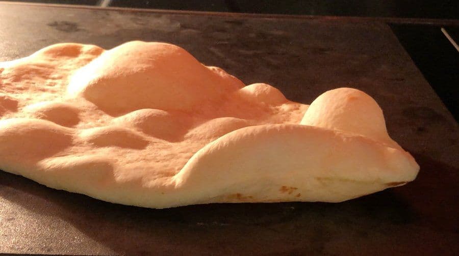 Freshly cooked naan bread with light brown spots on a dark surface, ready to be brushed with butter.