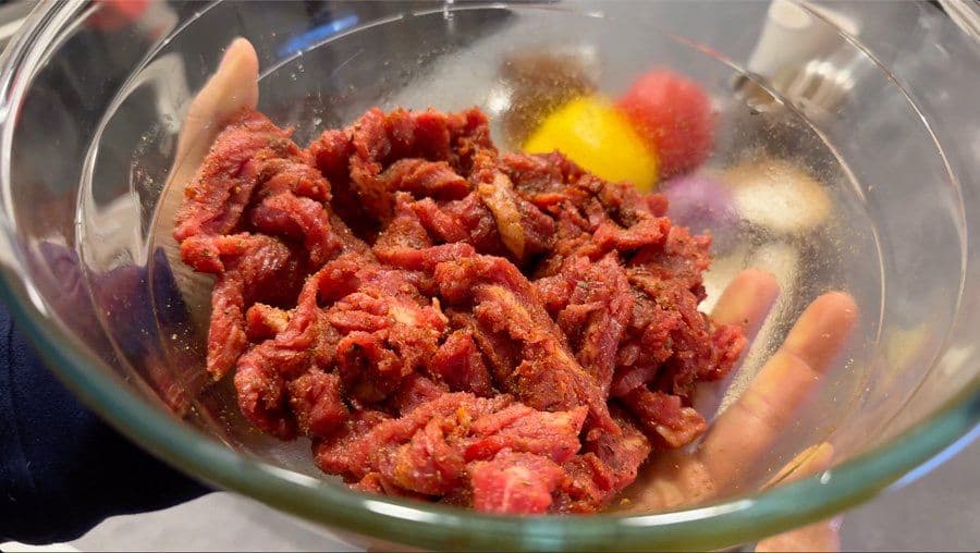 Raw flank steak tossed with Jamaican jerk seasoning and spices in a glass bowl, ready to marinate.