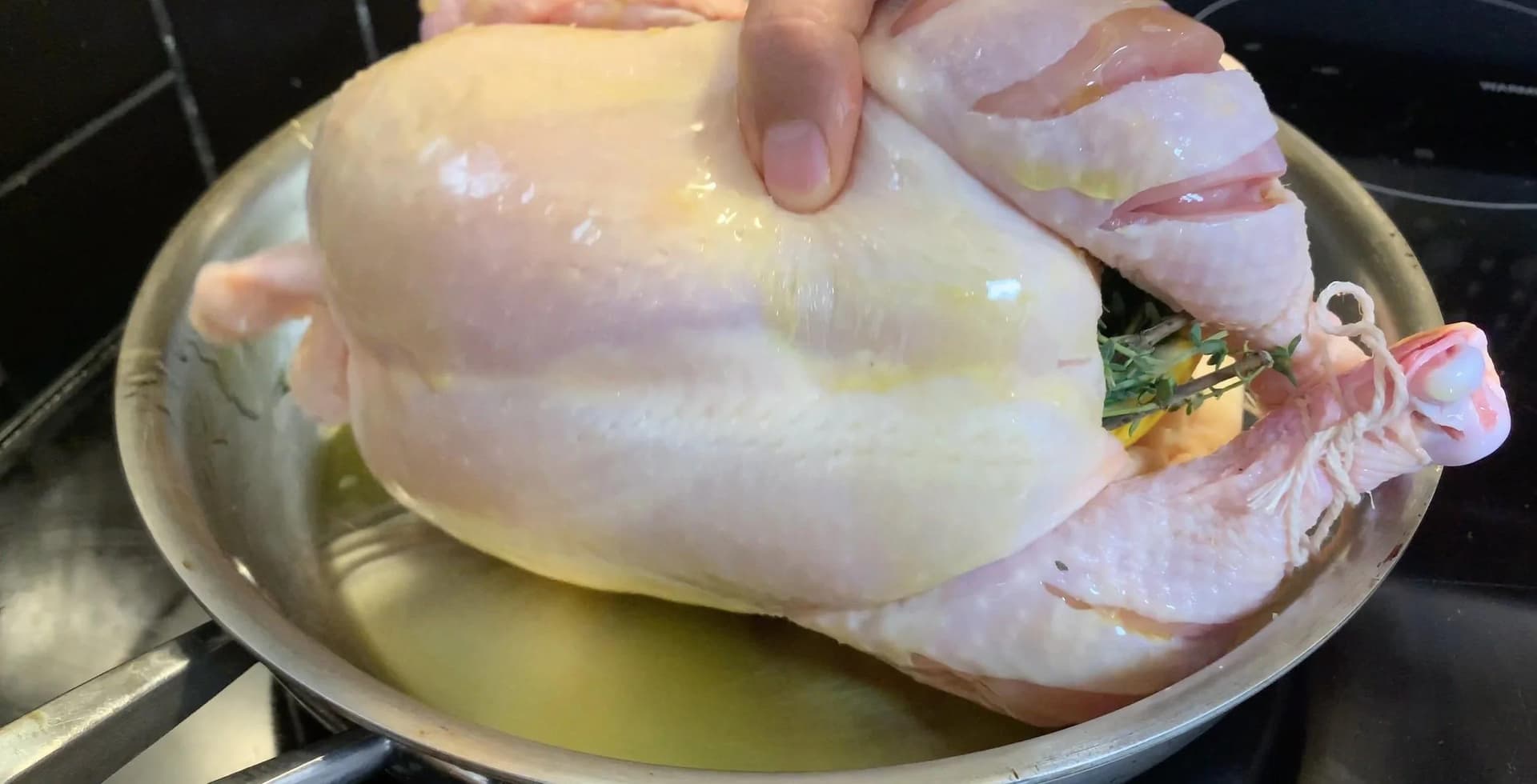 Raw chicken coated with olive oil in a stainless steel pan, trussed with twine and ready for roasting.
