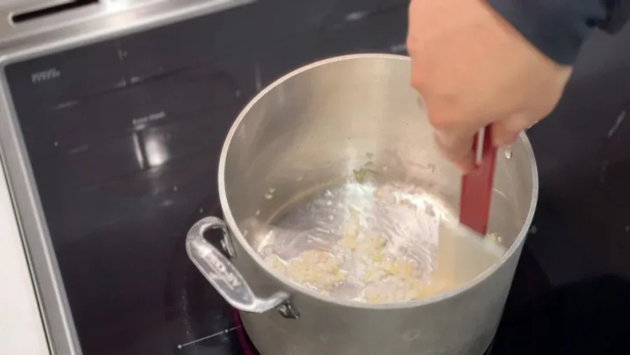 Stirring aromatics and spices into hot oil in a pot for peanut sauce base.
