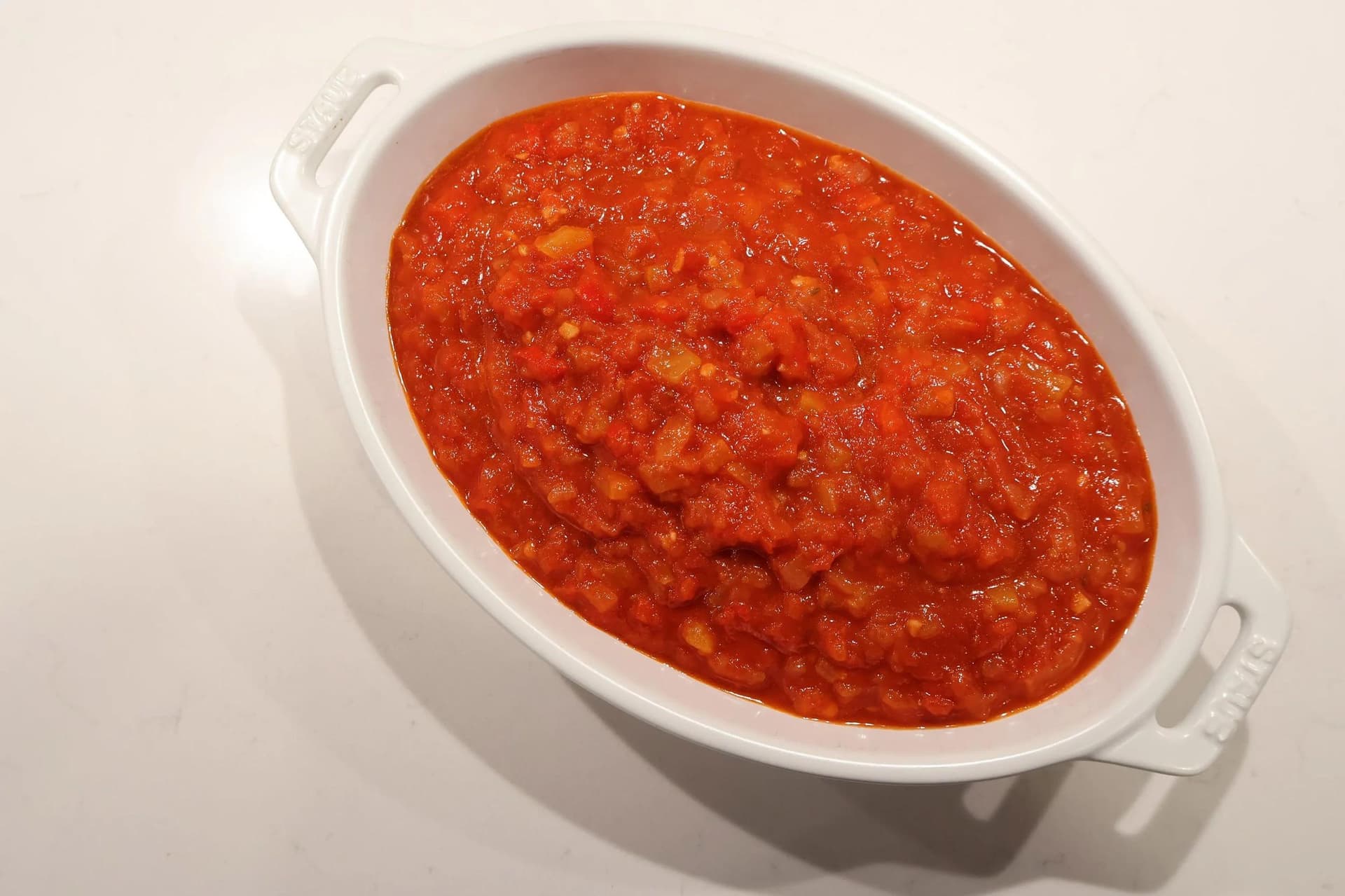 Chunky Basque piperade sauce in a white oval baking dish, with vibrant red tomatoes, peppers, and onions