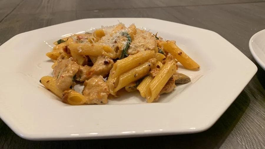 Spicy creamy chicken penne pasta with mushrooms and herbs on a white plate.