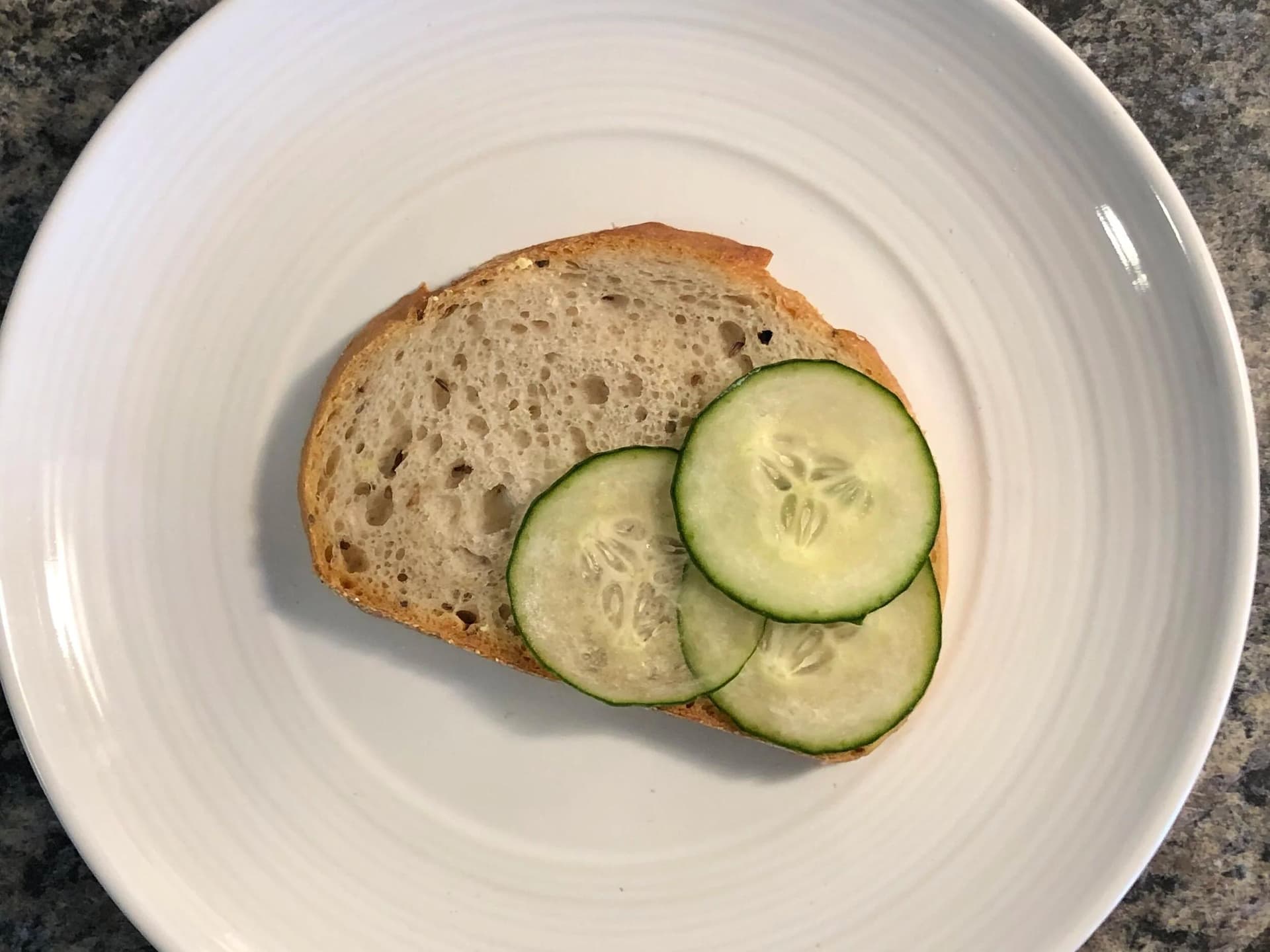 Toasted bread slice topped with overlapping cucumber slices on a white plate.