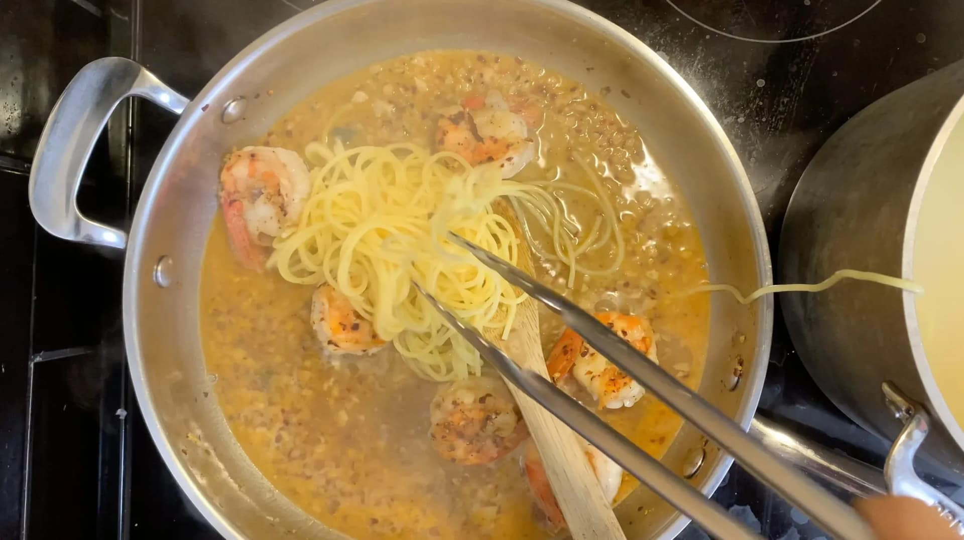 White wine lemon garlic shrimp scampi with spaghetti simmering in a pot, being stirred with tongs.