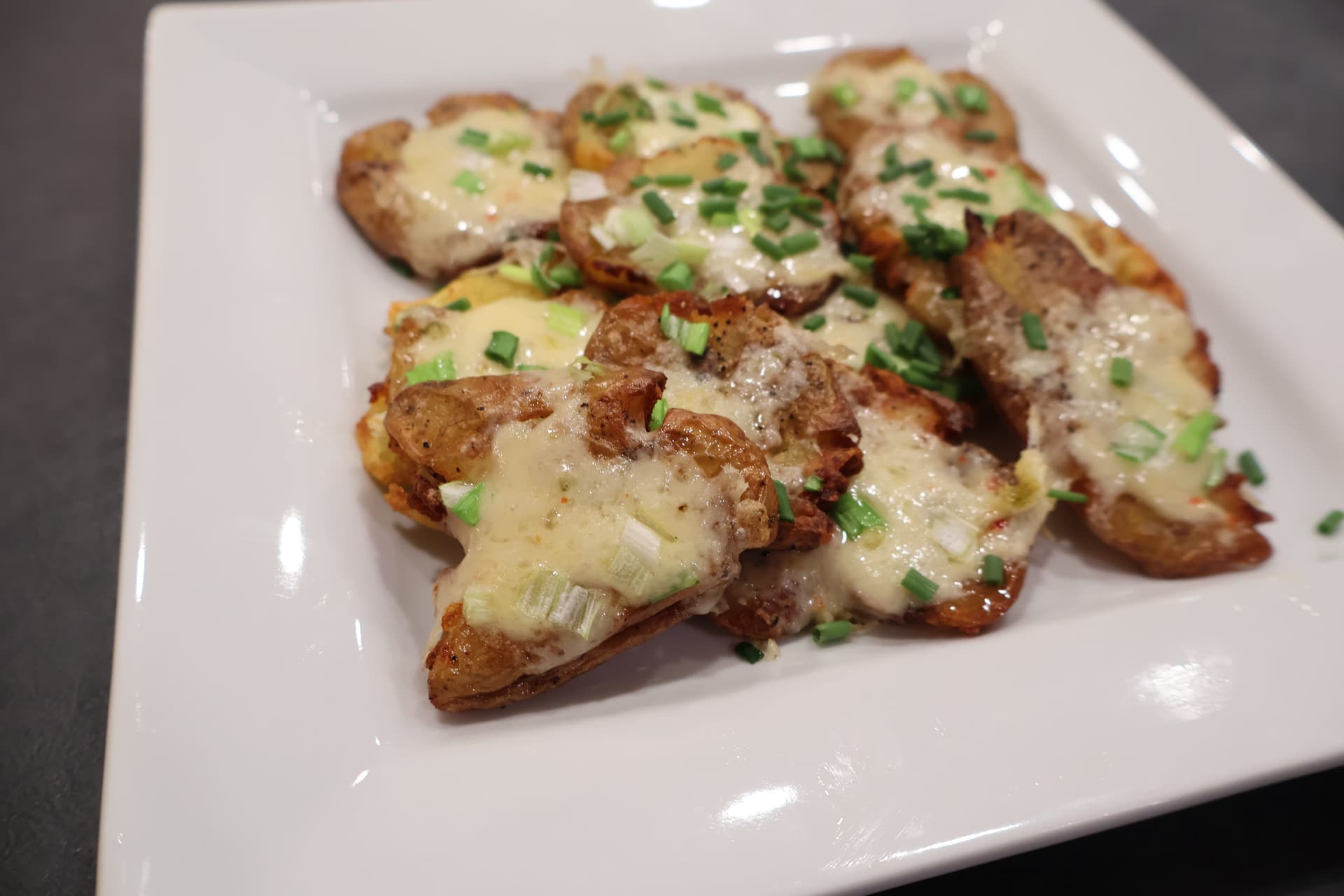 Crispy air fryer smashed potatoes topped with melted cheese and fresh chives on a white plate.