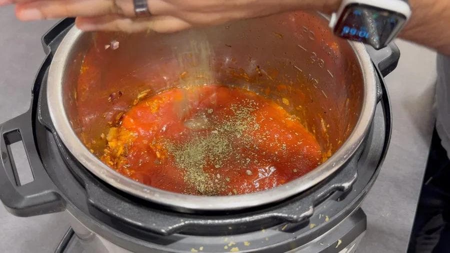 Instant Pot with red tomato-based sauce and sprinkled green spices during tikka masala preparation.