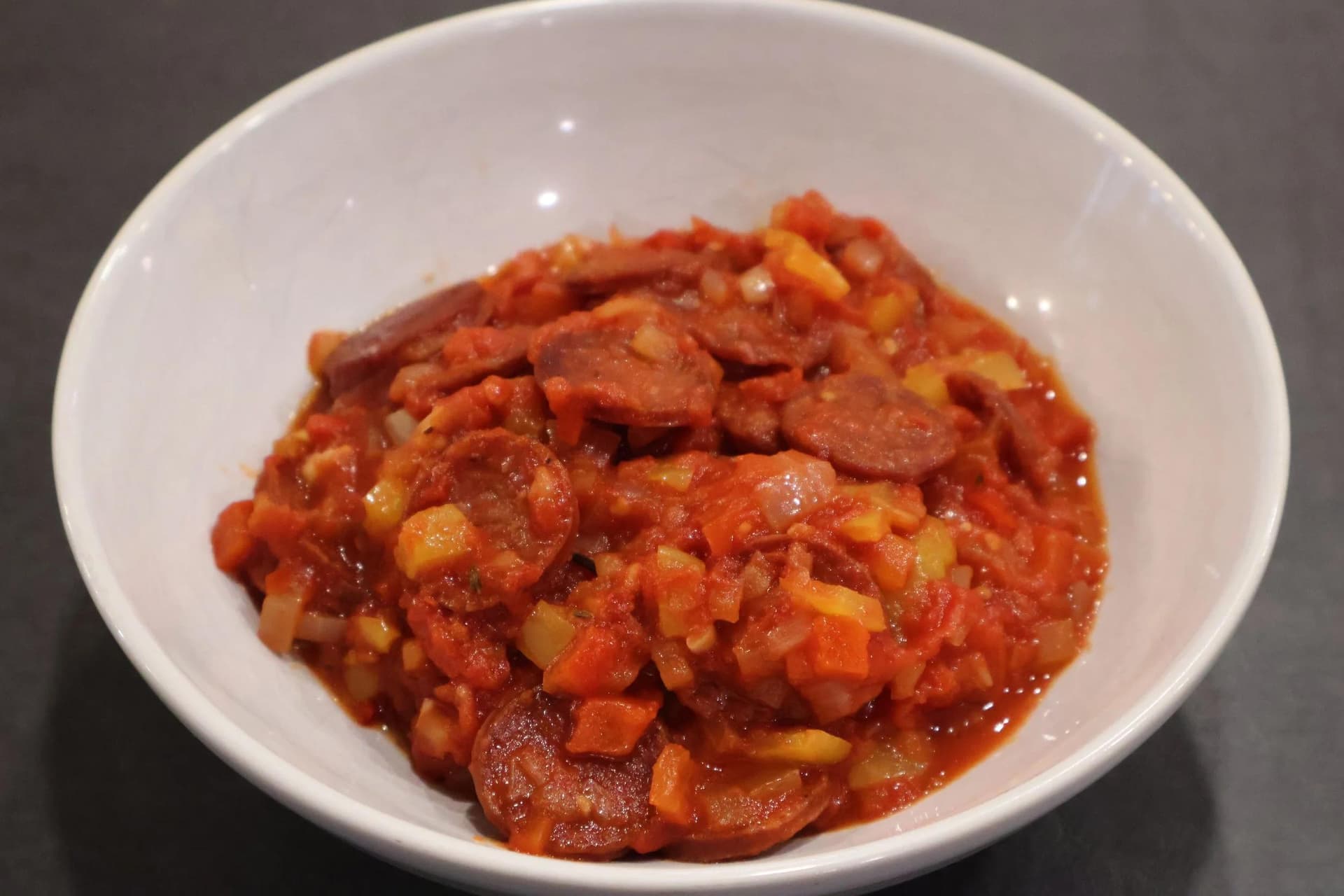 Basque piperade stew with sliced chorizo, tomatoes, peppers, and onions served in a white bowl