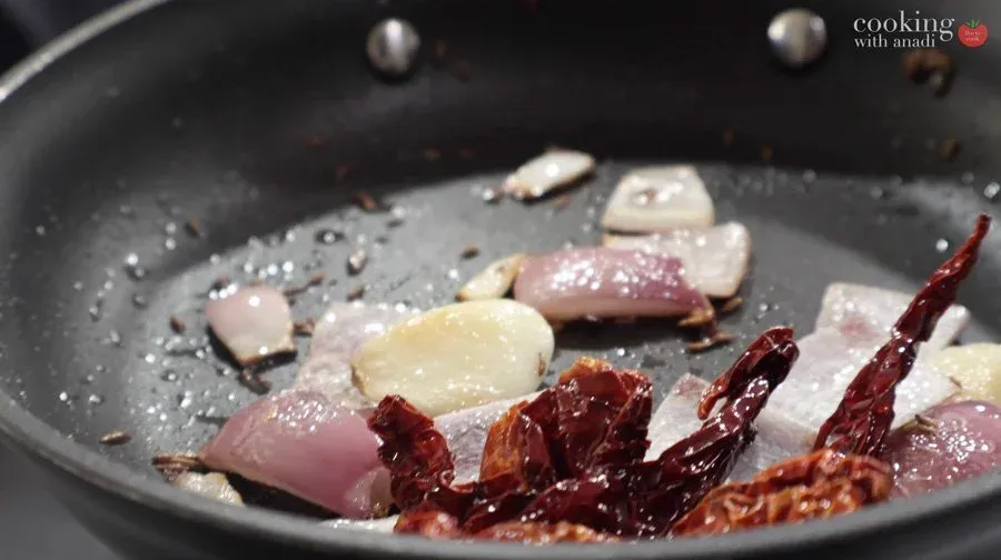 Sautéing onions, garlic, dried chilies, and cumin seeds in coconut oil in a dark pan for peanut chutney.